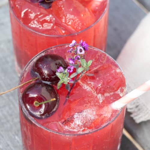 A cherry gin soda with cherries, edible flowers and a stripy straw.