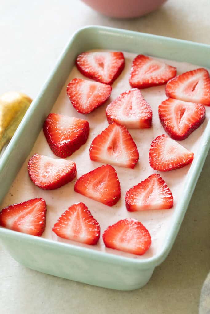 No-churn strawberry ice cream in a freezer-safe dish with fresh strawberries.