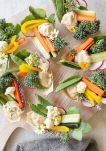 Hummus appetizer on small plates with freshly sliced vegetables.