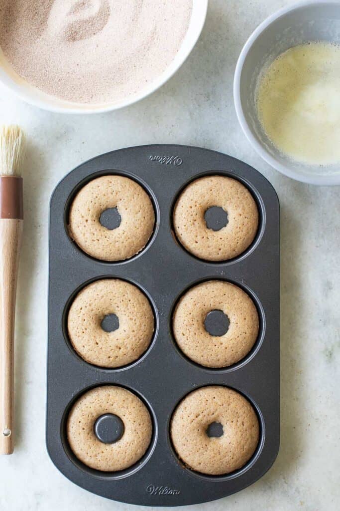 Baked apple cider donuts cooling in a donut pan.