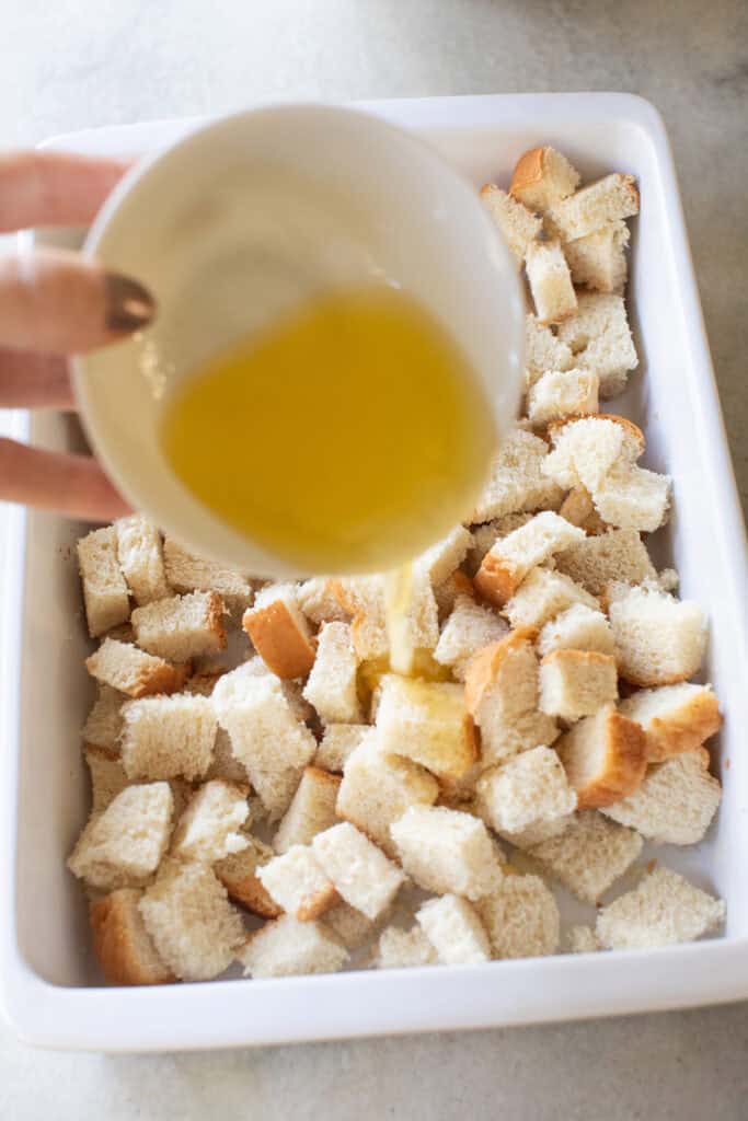 Pouring butter over bread cubes.