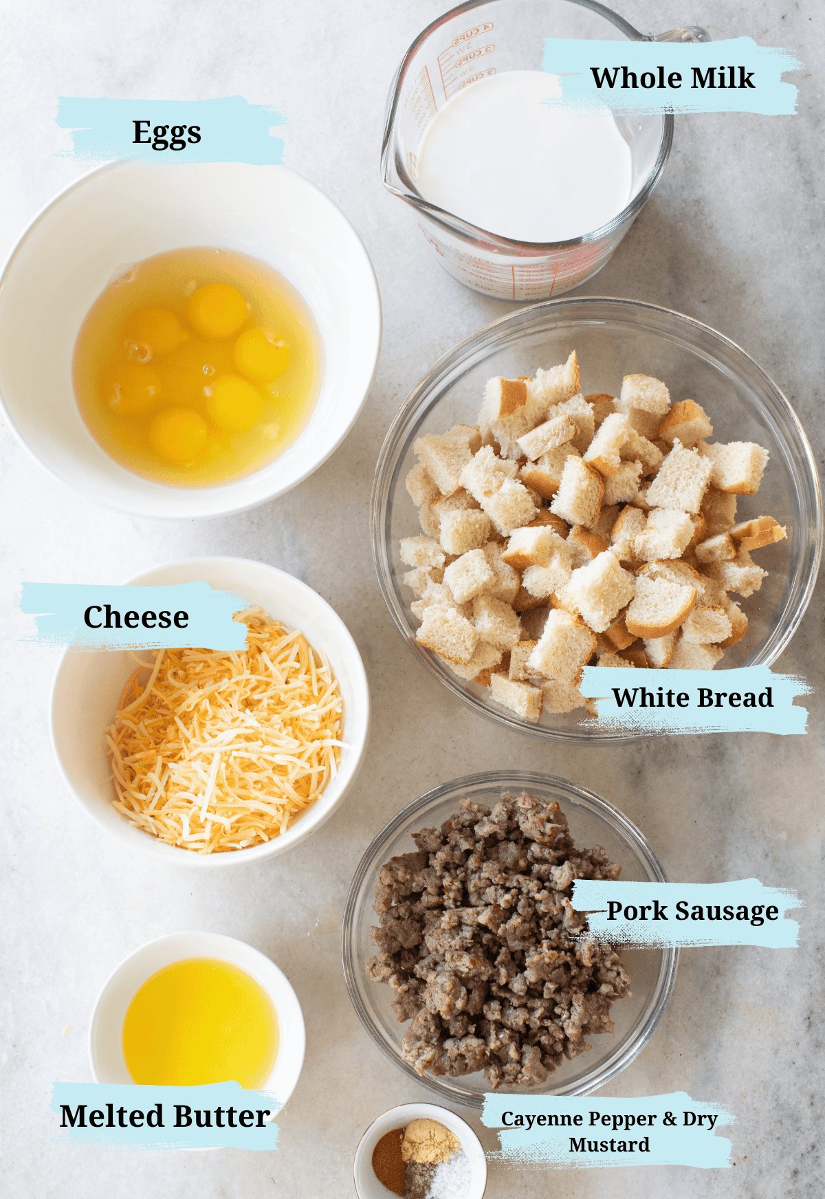 Cheese, eggs, pork sausage, bread, butter, milk, and spices in small bowls.