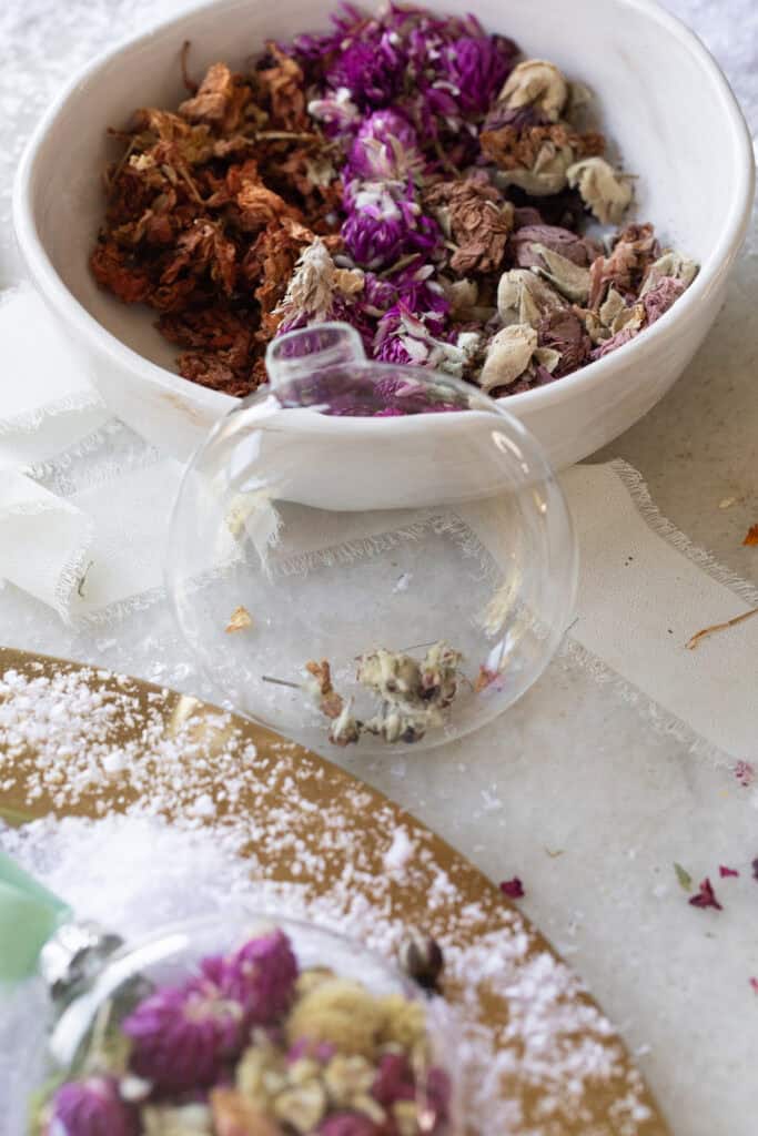 Filling a glass ornament with dried flowers. 