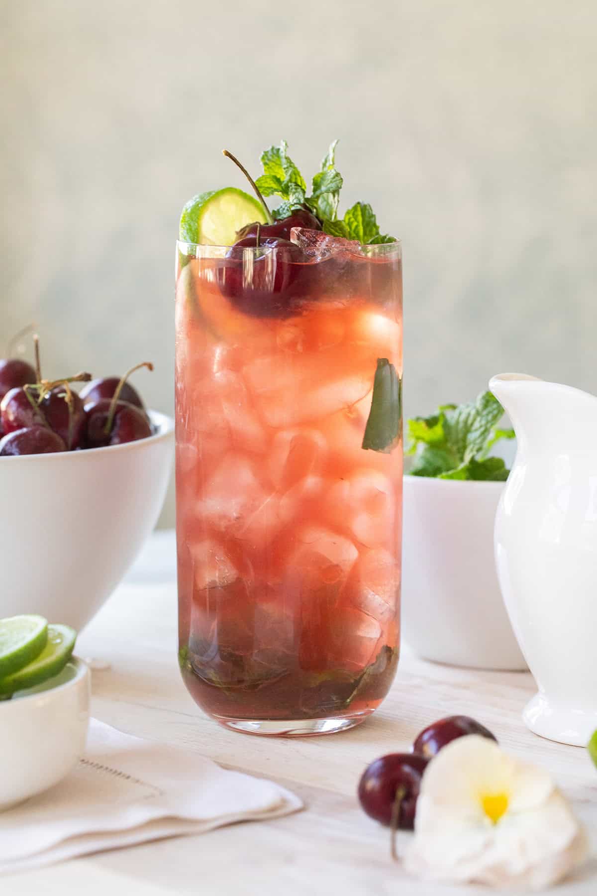 Cherry mojito in a tall glass with crushed ice, cherry juice, fresh mint and a lime wheel.