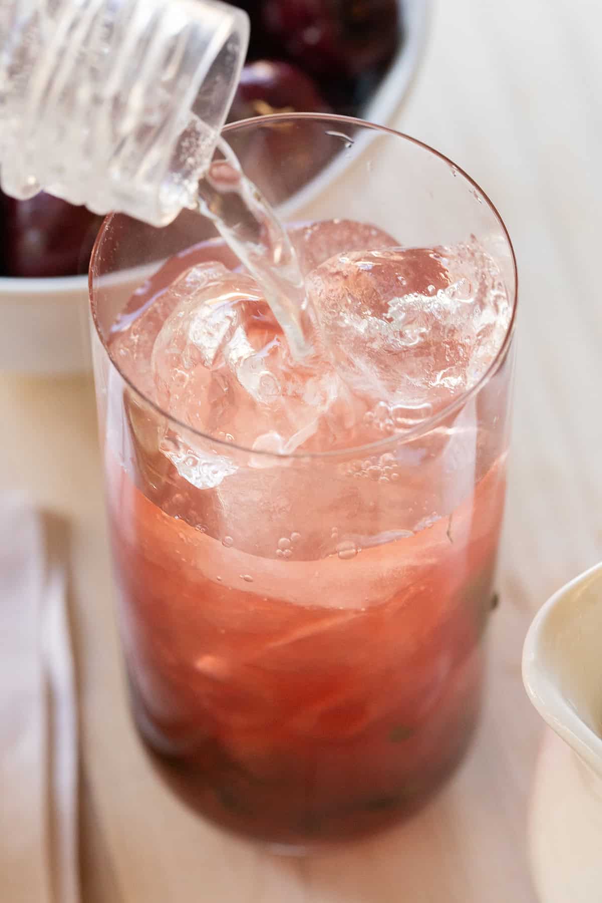 Pouring soda water into cherry juice to make a cherry mojito.