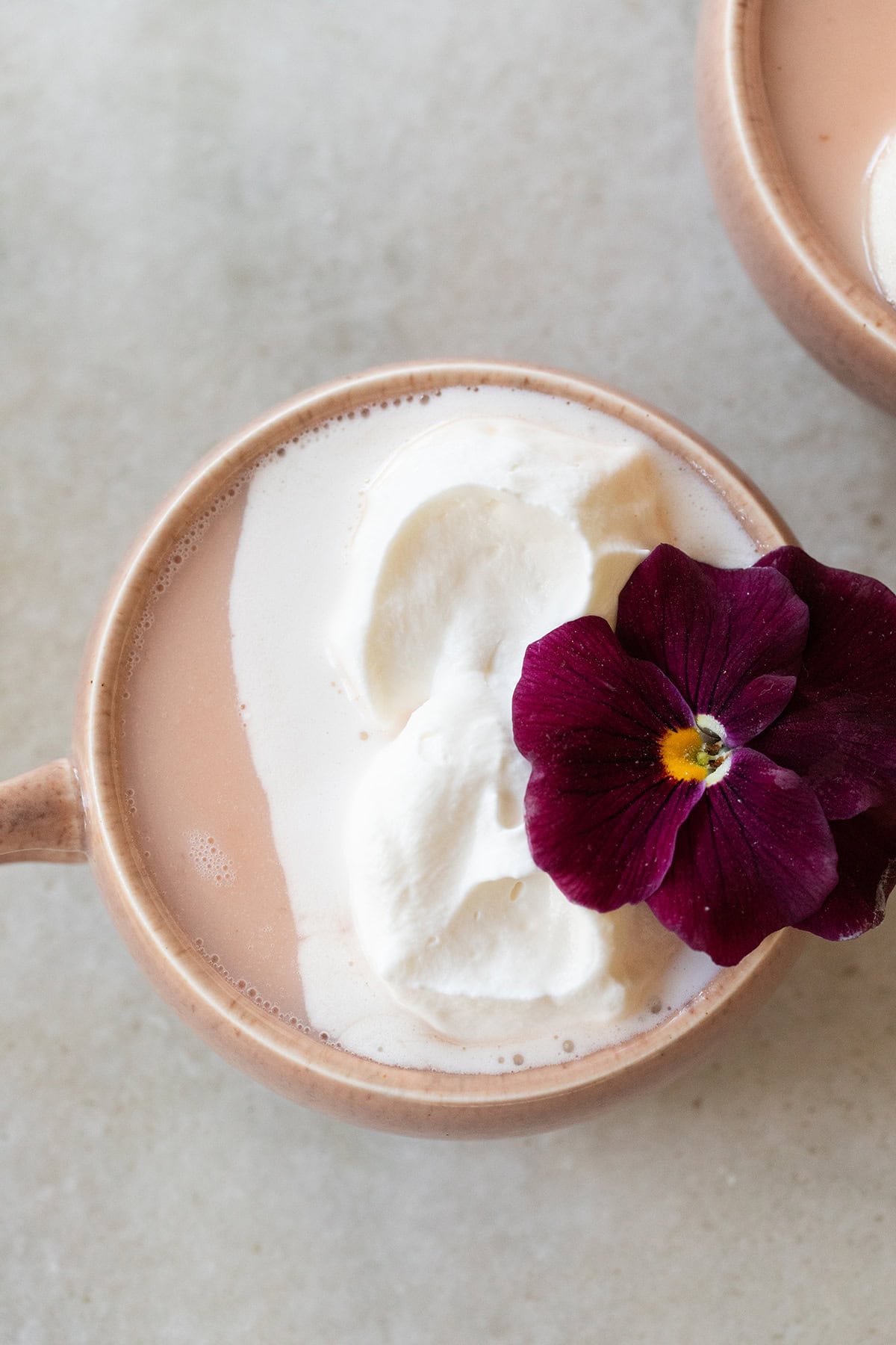 Pink hot chocolate with whipped cream, edible flower in a pink mug.