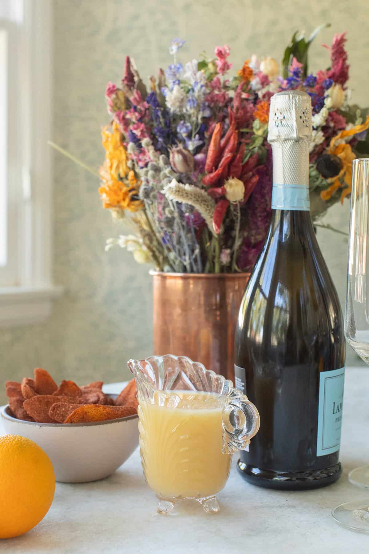 Prosecco, mango juice and candied mango on a table with flowers.