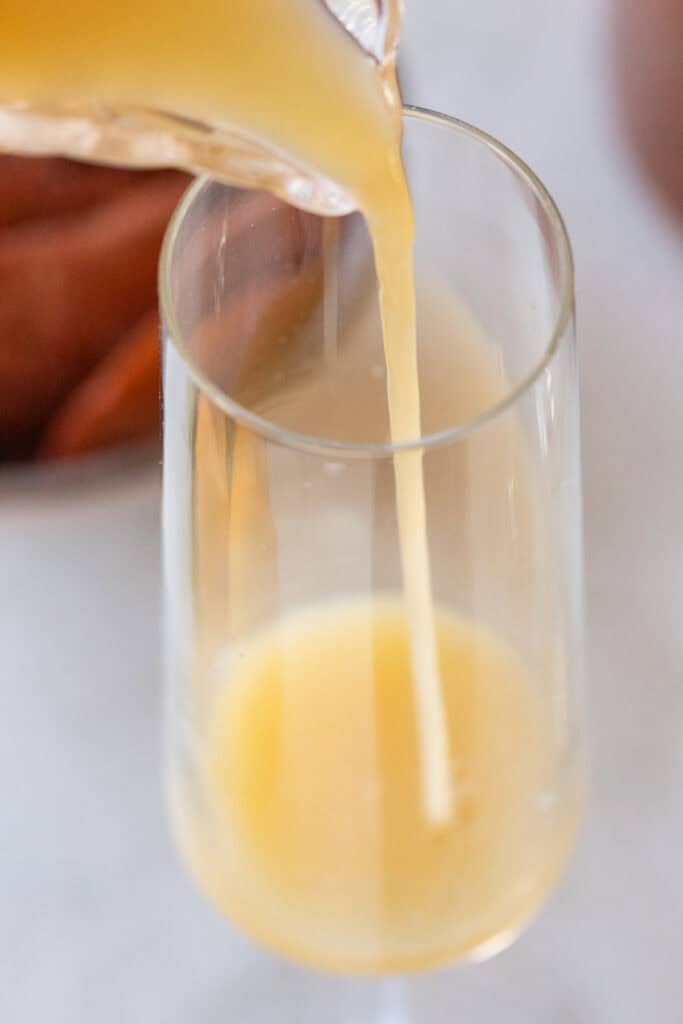 Pouring mango juice into a Champagne glass.