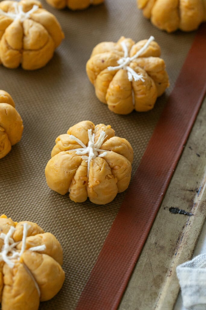 Tying baker’s twine around dough balls to shape pumpkin rolls.