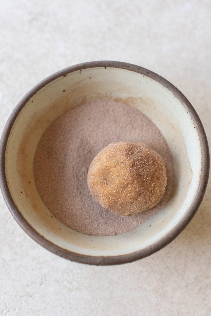 Rolling cookie dough balls in cinnamon sugar coating.