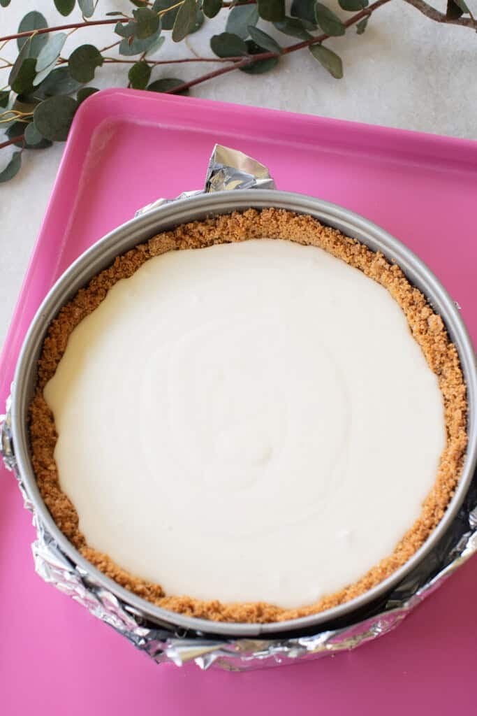 Cheesecake in graham cracker crust, on a baking sheet ready for a waterbath.