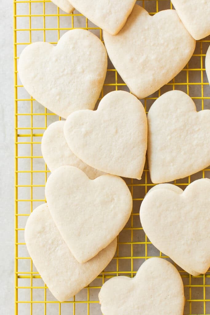 Classic cut out sugar cookies shaped as hearts on a cookie rack.