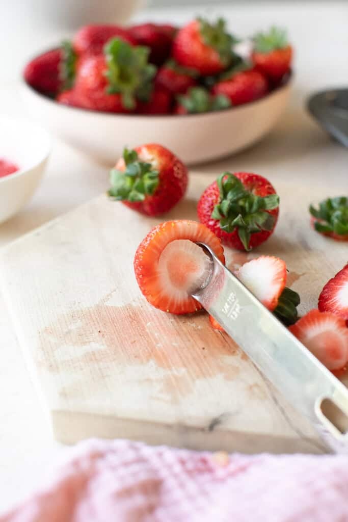 Fresh strawberries being sliced on a wooden cutting board for recipes or snacks.