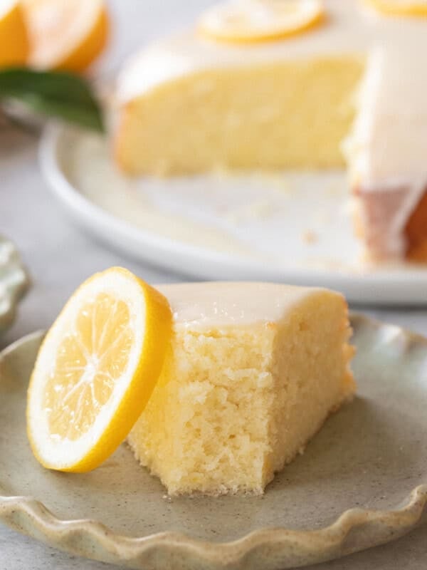 Moist lemon olive oil cake with a glaze and a slice of lemon on a plate.