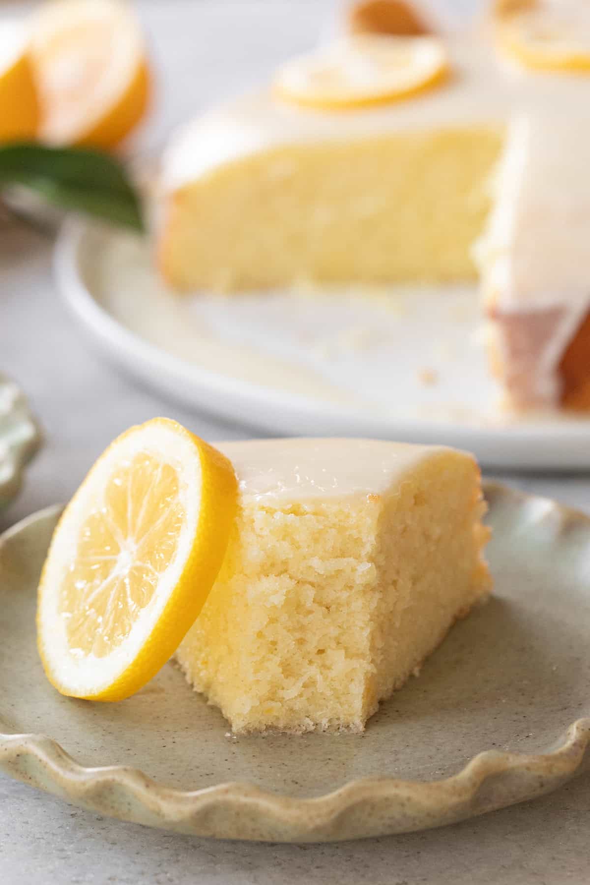 Moist lemon olive oil cake with a glaze and a slice of lemon on a plate.