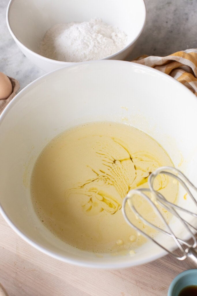 Olive oil drizzled into lemon olive oil cake batter in mixing bowl.