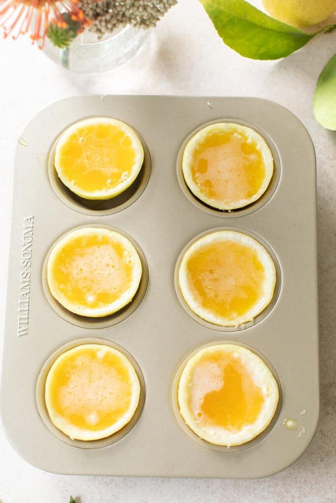 Pouring Hugo spritz jello mixture into halved lemon cups in a mini muffin pan.