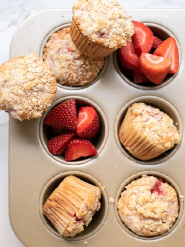 Strawberry muffins in a muffin tin with fresh strawberries.
