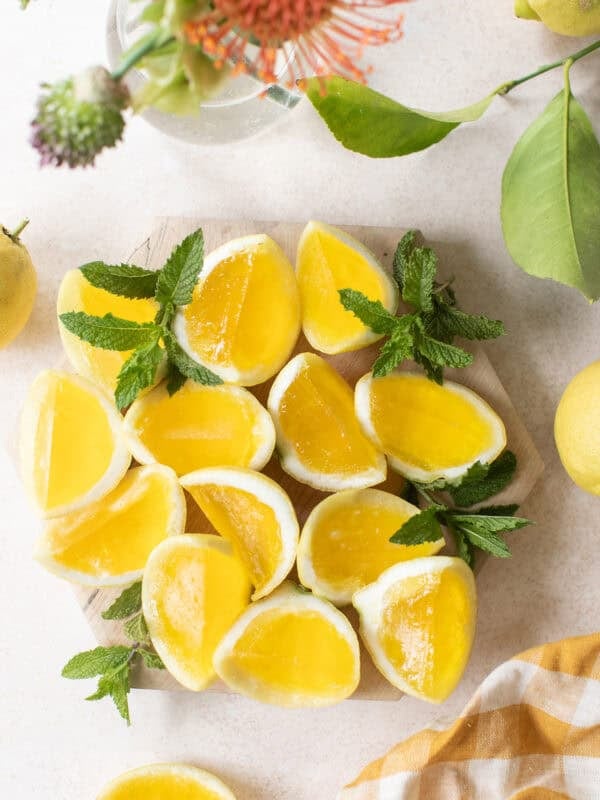 Hugo spritz jello shots on a table with lemons and flowers.