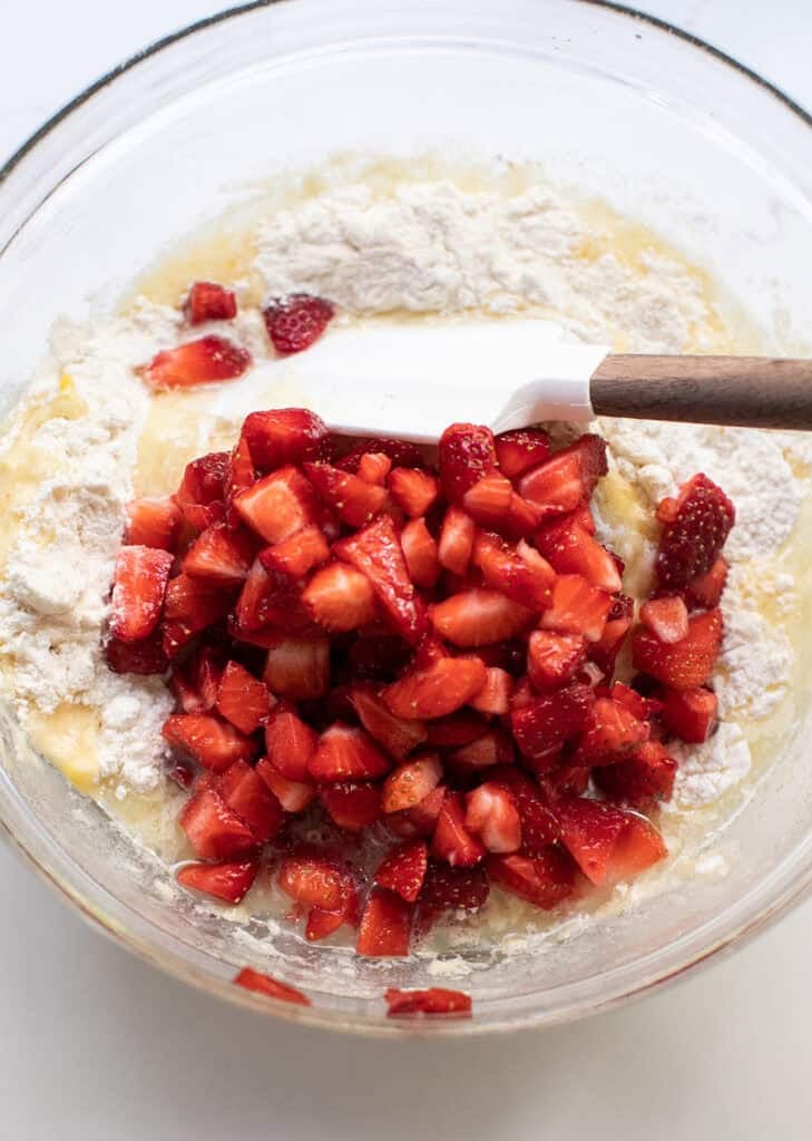 Strawberry muffin batter is being folded together with a spatula.