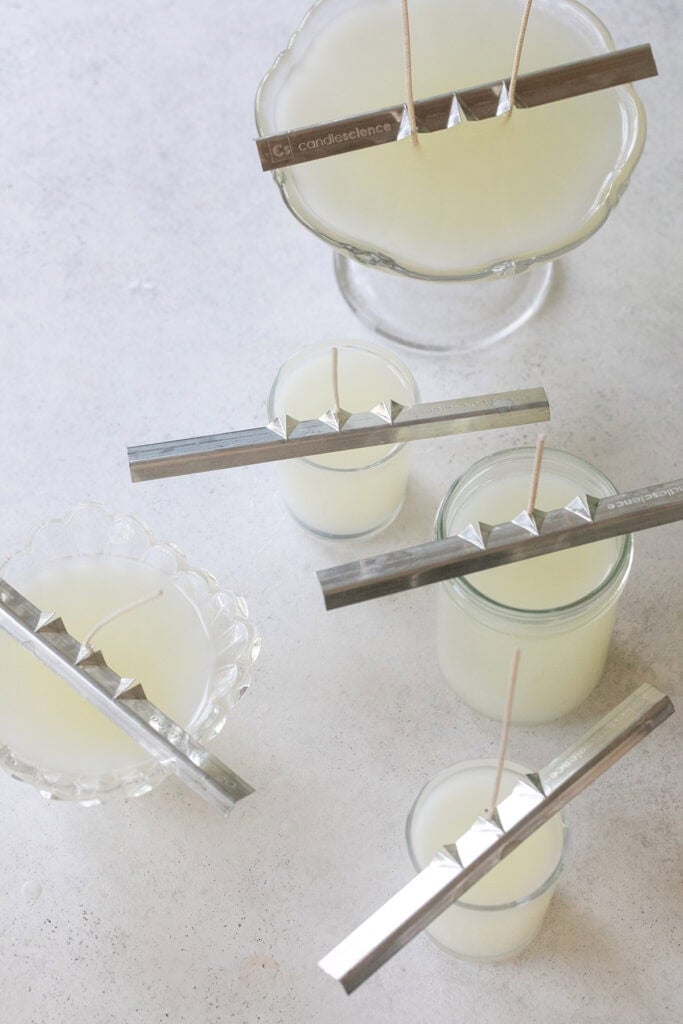Homemade candles curing with wick holders.