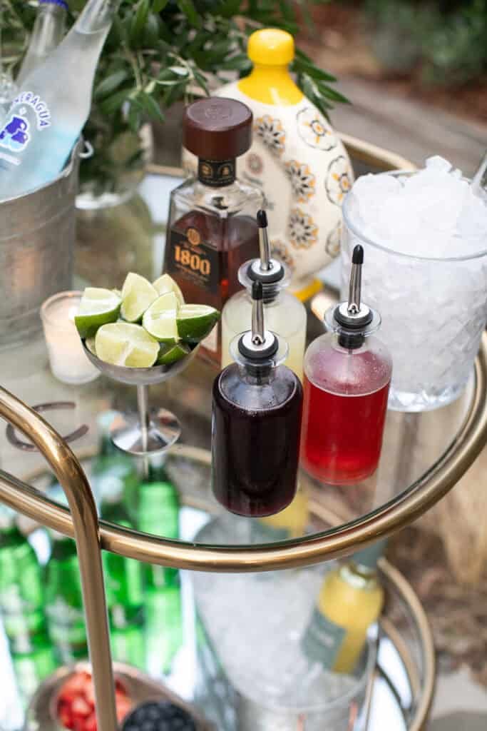 Homemade syrups on a bar cart with limes and tequila to make your own ranch water.