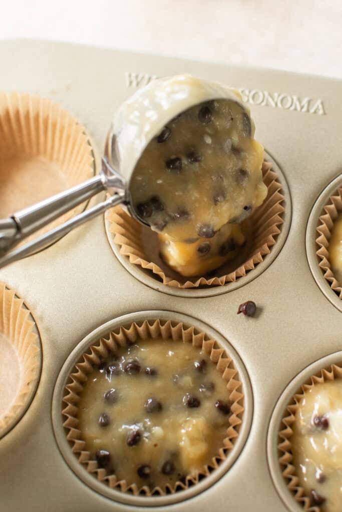 Scoping banana chocolate chip muffin batter into cupcake liners.